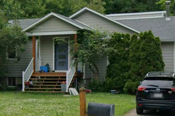Maison grise entourée d'arbres et voiture noire.
